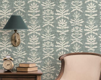 May include: A room interior featuring a teal and white floral patterned wallpaper. A dark teal wall lamp is mounted on the wall. A wooden nightstand holds a clock and books. A beige armchair is on the right.