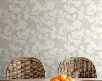 May include: A light beige wallpaper featuring a repeating white botanical leaf pattern, positioned behind a wooden table with a dark bowl of oranges and woven wicker chairs. The text APOSTROFO DESIGN is printed at the bottom of the image.
