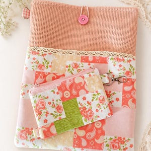 Könnte beinhalten: Eine rechteckige Tasche mit einem strukturierten pfirsichfarbenen Oberteil, einem rosa Knopfverschluss und einem Unterteil mit Blumen- und Paisley-Patchworkmuster. Eine kleinere passende Reißverschlusstasche mit Metallclip ist vorne befestigt.