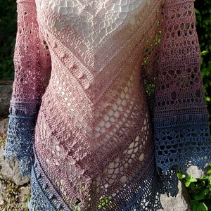 Peut inclure: Un châle en crochet fait à la main dans un dégradé de couleurs, du rose clair au bleu profond. Le motif ajouré présente des motifs complexes et un bord festonné. Le châle est présenté sur un mannequin.