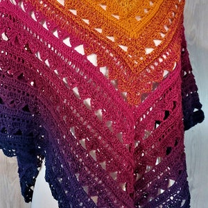 Peut inclure: Un châle crocheté à la main dans un dégradé de couleurs vives. Le châle passe du violet foncé en bas au magenta, à l'orange et enfin au jaune doré en haut. Le motif ajouré ajoute de la texture.