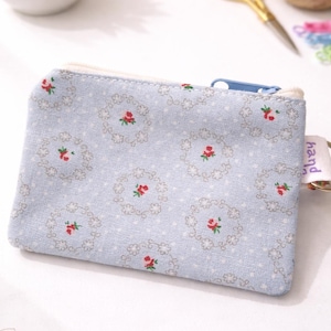 K&ouml;nnte beinhalten: Hellblaue Rei&szlig;verschlusstasche mit floralem Muster aus roten Rosen und grauen Akzenten. Die Tasche hat einen wei&szlig;en Rei&szlig;verschluss und ein kleines Etikett mit der Aufschrift "hand".
