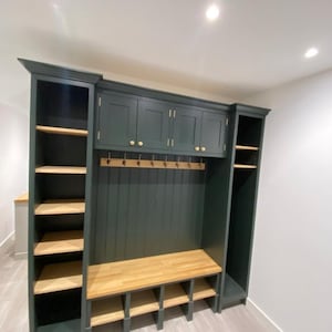 May include: A bespoke dark green hallway storage unit with a wooden bench, shoe storage, and overhead cupboards. The unit has open shelving on either side and brass hooks. The wooden bench and shelves have a natural finish, with a total width of approximately 200 cm.