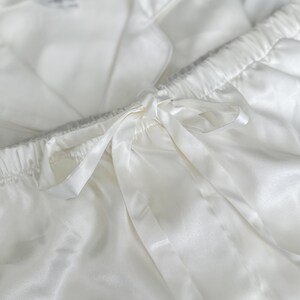 Puede incluir: Pantal&oacute;n de pijama de sat&eacute;n blanco con cintura el&aacute;stica y un lazo de cinta de sat&eacute;n.