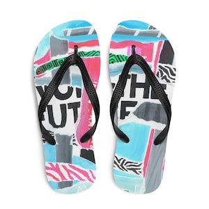 Op de afbeelding: Een paar teenslippers met een kleurrijk collage-ontwerp. Het ontwerp bevat blauwe, roze, grijze en witte elementen, met de woorden "YOU THE FUTURE" op de voetbedden. De bandjes zijn zwart.