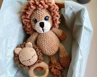 May include: A handmade crochet lion plush toy and matching rattle. The lion has a tan body, a brown mane, and blue eyes. The rattle features a lion face with a wooden ring. The set is presented in a box with light blue tissue paper.