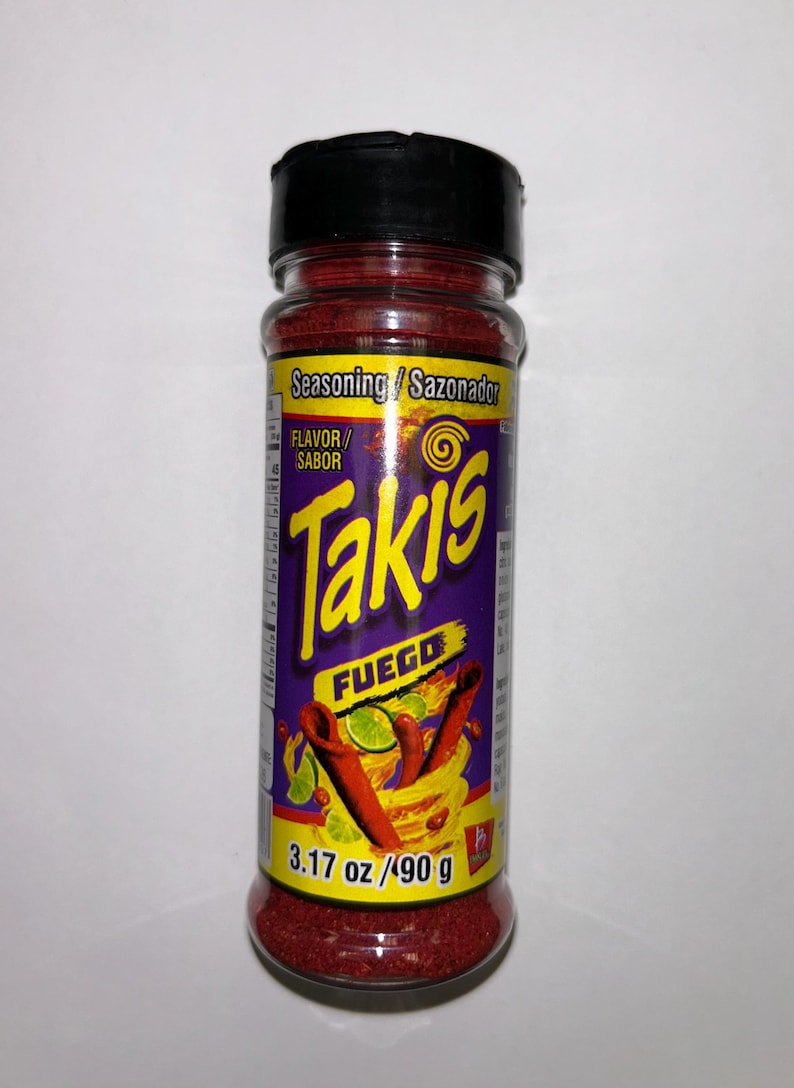 May include: A clear plastic bottle of Takis Fuego seasoning. The label is purple and yellow with the words "Takis Fuego" in large letters. The bottle contains 90 g of red seasoning.
