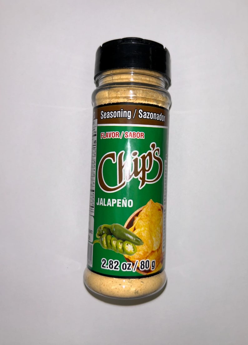 May include: A clear plastic bottle of jalape&ntilde;o seasoning with a black lid. The label features the text "Chips Jalape&ntilde;o" and a graphic of a jalape&ntilde;o pepper and chips. The bottle contains 80 g of seasoning.