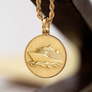 Può includere: Una collana con ciondolo circolare color oro caratterizzata da un design in rilievo di una nave da crociera che naviga sulle onde. Il ciondolo è sospeso a una catena a corda ritorta, con una finitura opaca sulla superficie e bordo perlato.