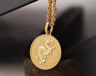 Peut inclure: Un collier en chaîne dorée avec un pendentif rond représentant un dragon détaillé.
