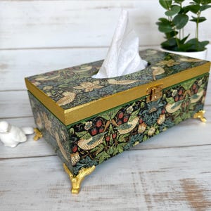 Peut inclure: Un couvre-boîte à mouchoirs avec un motif floral représentant des oiseaux et des baies. La boîte est en bois et possède une bordure dorée. Elle est dotée de quatre pieds dorés.