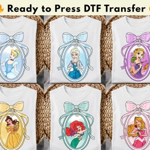以下が含まれることがあります： さまざまなプリンセスデザインの白いTシャツ。各シャツには、装飾的なリボンで飾られた楕円形のフレームの中に、異なるプリンセスの肖像画が描かれています。「Ready to Press DTF Transfer」というテキストが上部にあります。