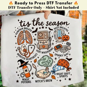 May include: A white DTF transfer sheet featuring a Halloween-themed medical graphic with the text 'tis the season'. Illustrations include a ribcage, ventilator, pulse oximeter, stethoscope with a ghost, pumpkin, and scrub caps with stars and bats.