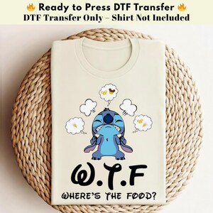 Könnte beinhalten: Ein beiges T-Shirt mit einer Grafik eines blauen Zeichentrickcharakters mit wütendem Gesichtsausdruck, umgeben von Sprechblasen mit Essensbildern. Der Text "W.T.F. WHERE'S THE FOOD?" ist darunter gedruckt. Der obere Teil des Bildes lautet "Ready to Press DTF Transfer".