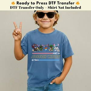 Puede incluir: Camiseta azul con un dise&ntilde;o de "Stitch Wars", que muestra personajes de dibujos animados y sables de luz. La camiseta tiene mangas cortas y cuello redondo. El texto "Ready to Press DTF Transfer" est&aacute; en la parte superior.