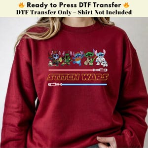 Puede incluir: Una sudadera granate con un gr&aacute;fico de personajes de Stitch vestidos como personajes de Star Wars. El texto "STITCH WARS" est&aacute; debajo de los personajes, con dise&ntilde;os de sables de luz rojos y azules.