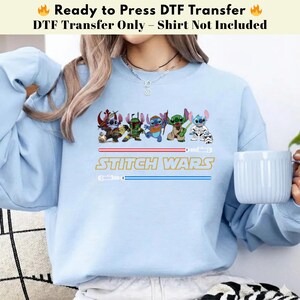 Puede incluir: Sudadera azul claro con un dise&ntilde;o de "Stitch Wars" que presenta personajes de dibujos animados y sables de luz. El texto "Ready to Press DTF Transfer" est&aacute; en la parte superior. Solo transferencia DTF, camisa no incluida.