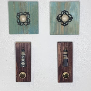 Pode incluir: Quatro ganchos de parede de madeira com botões decorativos. Dois ganchos são pintados de azul e apresentam um design metálico com um botão branco. Os outros dois ganchos são pintados de marrom e apresentam um design de farol com um botão dourado.