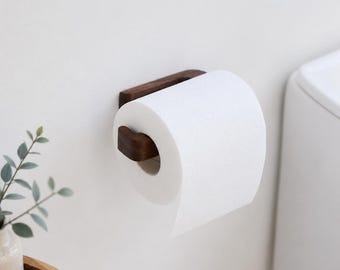 May include: A wall-mounted toilet paper holder crafted from dark brown wood, featuring a horizontal arm that supports a standard roll of white toilet paper. The holder has a rectangular base plate attached to the wall with a curved arm extending outward.