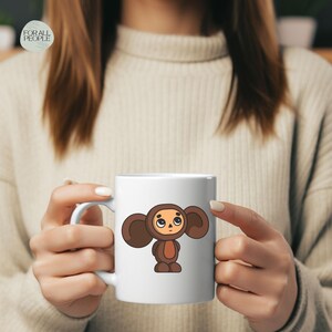 May include: White ceramic mug with a cartoon illustration of a brown furry character with large ears and a sad expression. The character is wearing a brown jumpsuit.