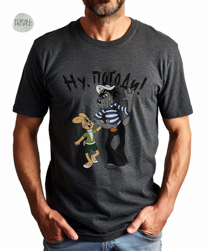 May include: A dark grey t-shirt with a cartoon image of a wolf and a rabbit. The wolf is wearing a sailor hat and striped shirt. The text "Ну, погоди!" is printed on the shirt.