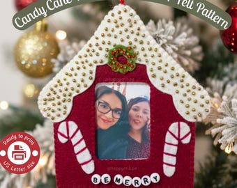 May include: A house-shaped felt ornament in deep red with a white roof decorated with gold beads. It features a central photo window, two white and red candy cane appliqués, a small green wreath, and the text BE MERRY in white letter beads.