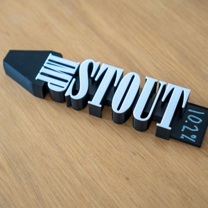 May include: A black and silver 3D printed sign that reads "STOUT 10.2%".