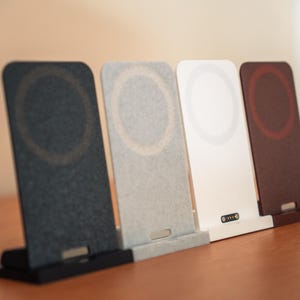 Può includere: Quattro supporti di ricarica wireless verticali disposti in fila. I supporti sono grigio scuro, grigio chiaro, bianco e rosso scuro. Ogni supporto rettangolare presenta un'area di ricarica magnetica circolare sulla parte anteriore e una base.