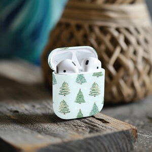 K&ouml;nnte beinhalten: Ein wei&szlig;es Airpods-Case mit hellblauem Hintergrund und einem Muster aus gr&uuml;nen Weihnachtsb&auml;umen. Das Case ist ge&ouml;ffnet und die beiden wei&szlig;en Airpods sind im Inneren sichtbar.