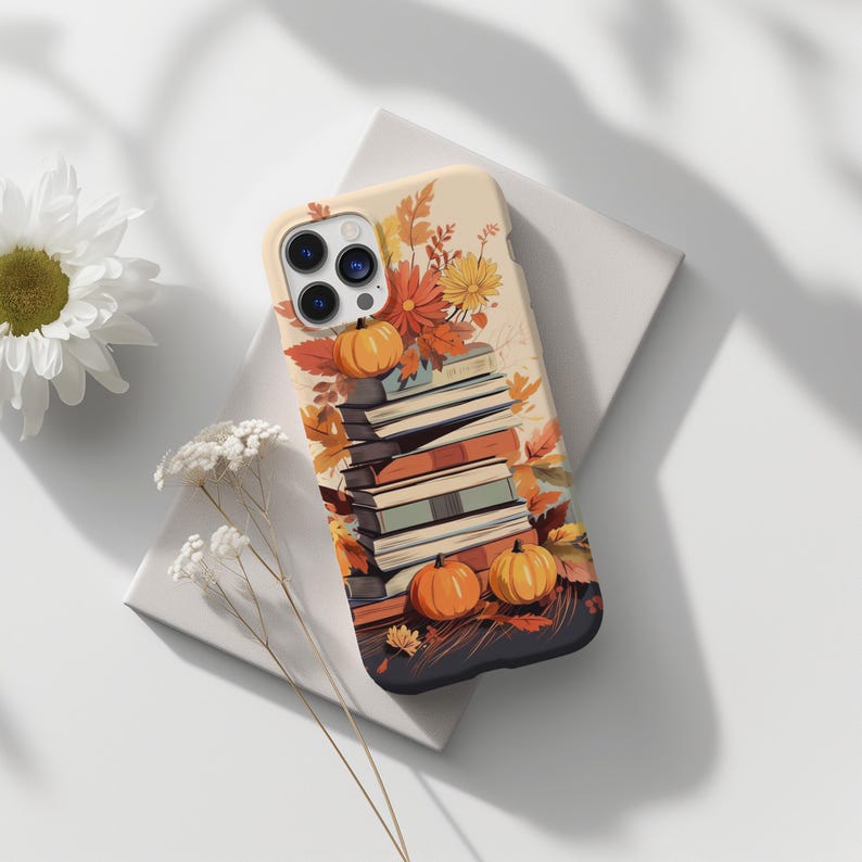 May include: A phone case with a fall-themed design featuring a stack of books, pumpkins, and autumn leaves. The case is black with a cream background.