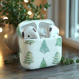 K&ouml;nnte beinhalten: Wei&szlig;e kabellose Ohrh&ouml;rer in einem wei&szlig;en Etui mit einem Weihnachtsbaum-Muster. Das Etui hat einen Klappdeckel und eine kleine &Ouml;ffnung zum Aufladen.