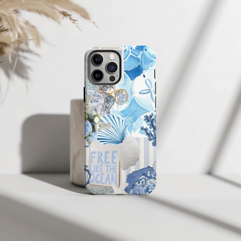 May include: A white iPhone case with a collage of blue and white images, including seashells, flowers, and a sign that says "Free Like The Ocean".