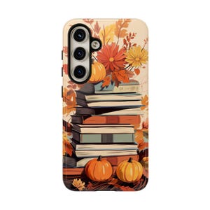 May include: A phone case with a fall-themed design featuring a stack of books, pumpkins, and autumn leaves. The case has a cream background with a floral pattern.
