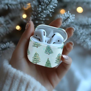K&ouml;nnte beinhalten: Wei&szlig;es drahtloses Ohrh&ouml;rer-Etui mit einem Weihnachtsbaum-Muster. Das Etui ist ge&ouml;ffnet und die Ohrh&ouml;rer befinden sich darin.