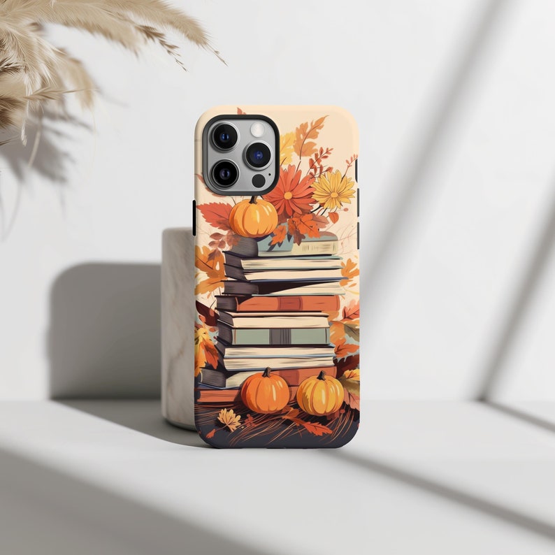 May include: A phone case with a fall-themed design featuring a stack of books, pumpkins, and autumn leaves. The case is designed for an iPhone.