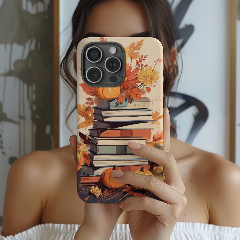 May include: A phone case with a fall-themed design featuring a stack of books, autumn leaves, and pumpkins. The case is cream-colored with a brown border.