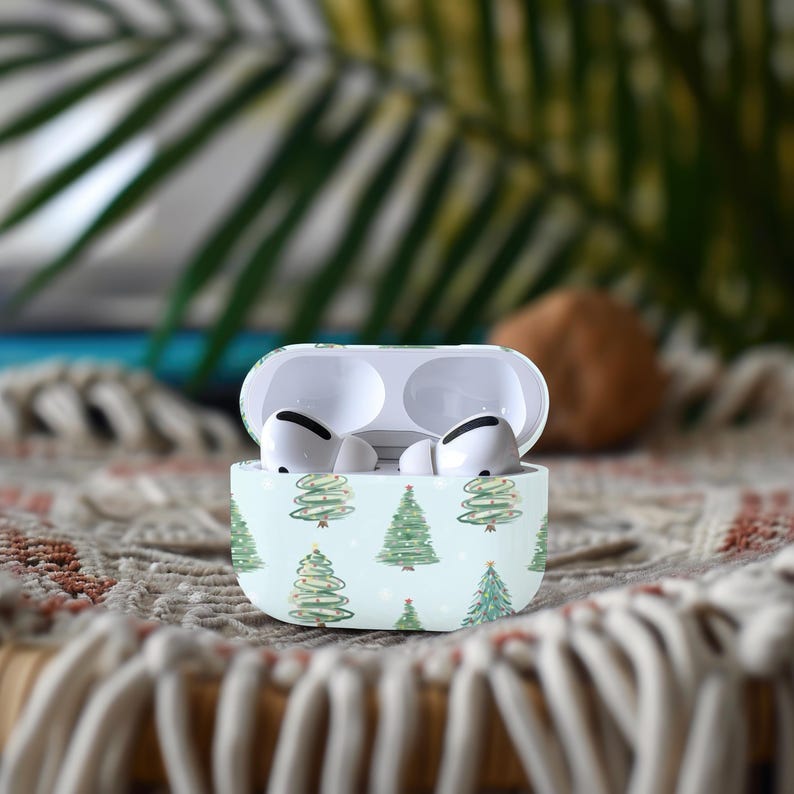 K&ouml;nnte beinhalten: Wei&szlig;e Airpods-H&uuml;lle mit Weihnachtsbaum-Design. Die H&uuml;lle hat einen hellblauen Hintergrund mit gr&uuml;nen Weihnachtsb&auml;umen und wei&szlig;en Schneeflocken.