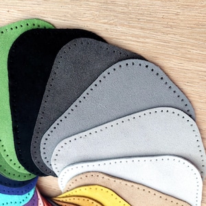 May include: A selection of felt patches in various colours, including green, black, grey, and white. The patches are all shaped like a rounded rectangle and have a stitched edge.