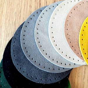 Peut inclure: Une collection de bases en cuir rondes et colorées, dans des tons variés : noir, vert, bleu, gris, beige et or. Chaque base est percée de trous espacés régulièrement sur le pourtour, pour des projets créatifs.