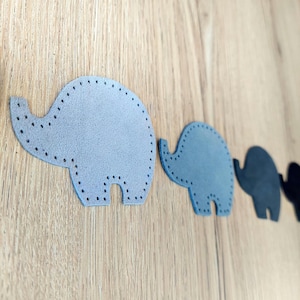 Op de afbeelding: Vier vilten olifantvormen op een rij. De eerste olifant is lichtgrijs, de tweede is blauw, de derde is zwart en de vierde is donkergrijs.