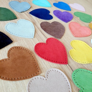 Könnte beinhalten: Sortiment an Filzherzen in verschiedenen Farben, darunter Rot, Blau, Grün, Gelb, Orange, Braun und Beige. Die Herzen sind mit einem dekorativen Stich um die Ränder genäht.