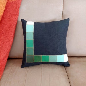 May include: Black pillow with a green and white geometric border. The border is made of squares of different shades of green and white.