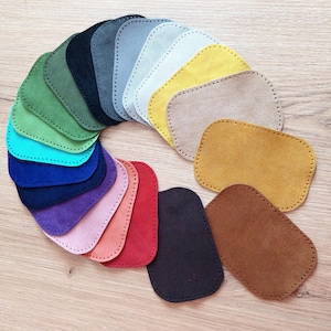 Puede incluir: Un conjunto de 18 parches de cuero de gamuza en varios colores, dispuestos en un círculo. Los parches son de forma ovalada y tienen un borde cosido.