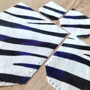 Può includere: Un set di quattro sottobicchieri e un pezzo di materiale più grande con un motivo a strisce zebrate. Il design presenta strisce bianche, nere e blu. I sottobicchieri e il materiale sembrano essere realizzati in un materiale strutturato, possibilmente pelle o cuoio.