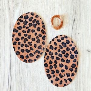 Puede incluir: Dos círculos de tela marrón y negro con estampado de leopardo sobre una superficie de madera clara. Un rollo de alambre de cobre se encuentra en la parte superior central de la imagen.