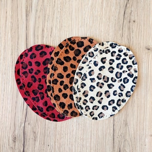 Puede incluir: Tres parches redondos de tela con un diseño de estampado de leopardo. Los parches son en tonos rojo, marrón y beige.