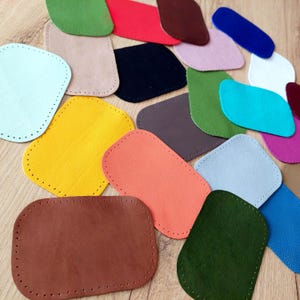 May include: A collection of rectangular leather patches with rounded corners and pre-punched stitching holes along the edges. The patches are available in a variety of solid colors including red, yellow, orange, green, blue, brown, black, and white.