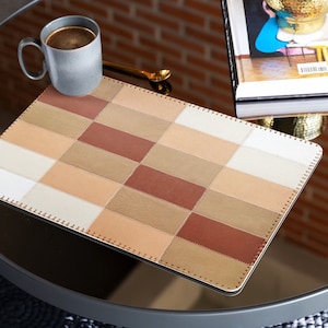 Könnte beinhalten: Ein rechteckiger Platzdeckchen aus Leder mit einem karierten Muster in Braun-, Beige- und Weißtönen. Das Platzdeckchen hat einen genähten Rand.