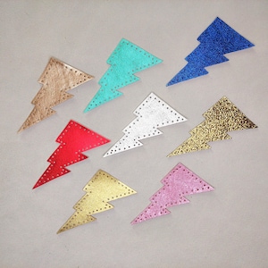 May include: A collection of colorful, metallic lightning bolt patches. The patches are in various colors, including gold, silver, red, blue, and pink. Each bolt has a stitched border with small holes. These patches are ideal for adding flair to clothing or accessories.