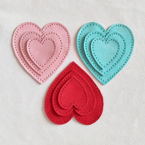 Puede incluir: Tres corazones de fieltro de diferentes tamaños, cada uno con un corazón más pequeño en su interior. Los corazones son rosa, azul y rojo.
